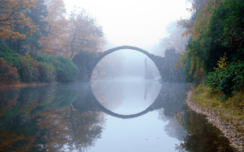 Bridge connecting two pieces of land and forming a circle with the reflection in the water to signify bridging a gap.